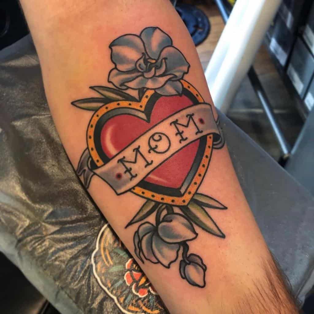 Tattoo of a heart adorned with a "Mom" banner and surrounded by vibrant flowers, beautifully inked on a person's arm