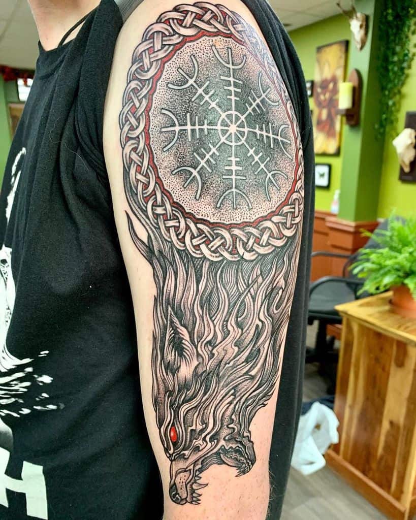 Tattoo of a wolf with red eyes and a Nordic symbol on an arm, surrounded by intricate knotwork