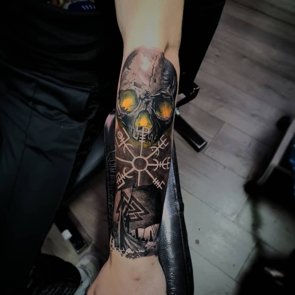 A striking forearm tattoo featuring a glowing skull with the Vegvisir symbol, accompanied by a Viking ship and Valknut design