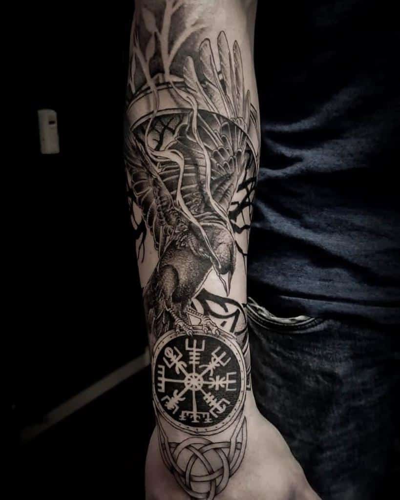 A Nordic forearm tattoo featuring a raven in flight, the Vegvisir symbol, and intricate knotwork, set against a backdrop of tree branches