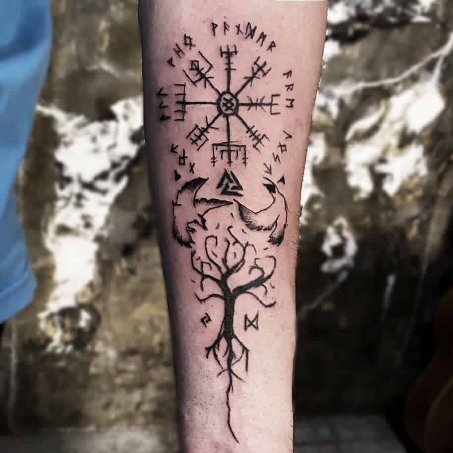 A Nordic forearm tattoo featuring the Vegvisir symbol, two wolves encircling the Valknut, and Yggdrasil with runes along its roots