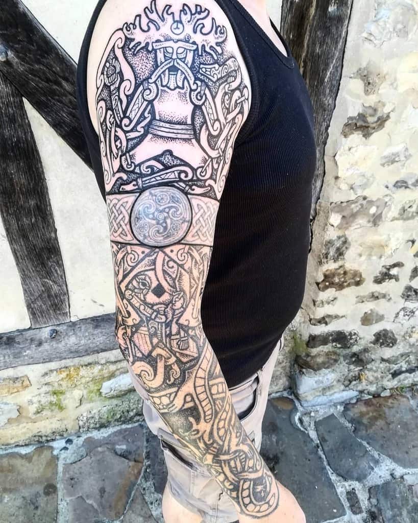 A full-sleeve tattoo featuring intricate Nordic designs, including knotwork, mythical figures, a circular triskelion symbol, and detailed geometric patterns
