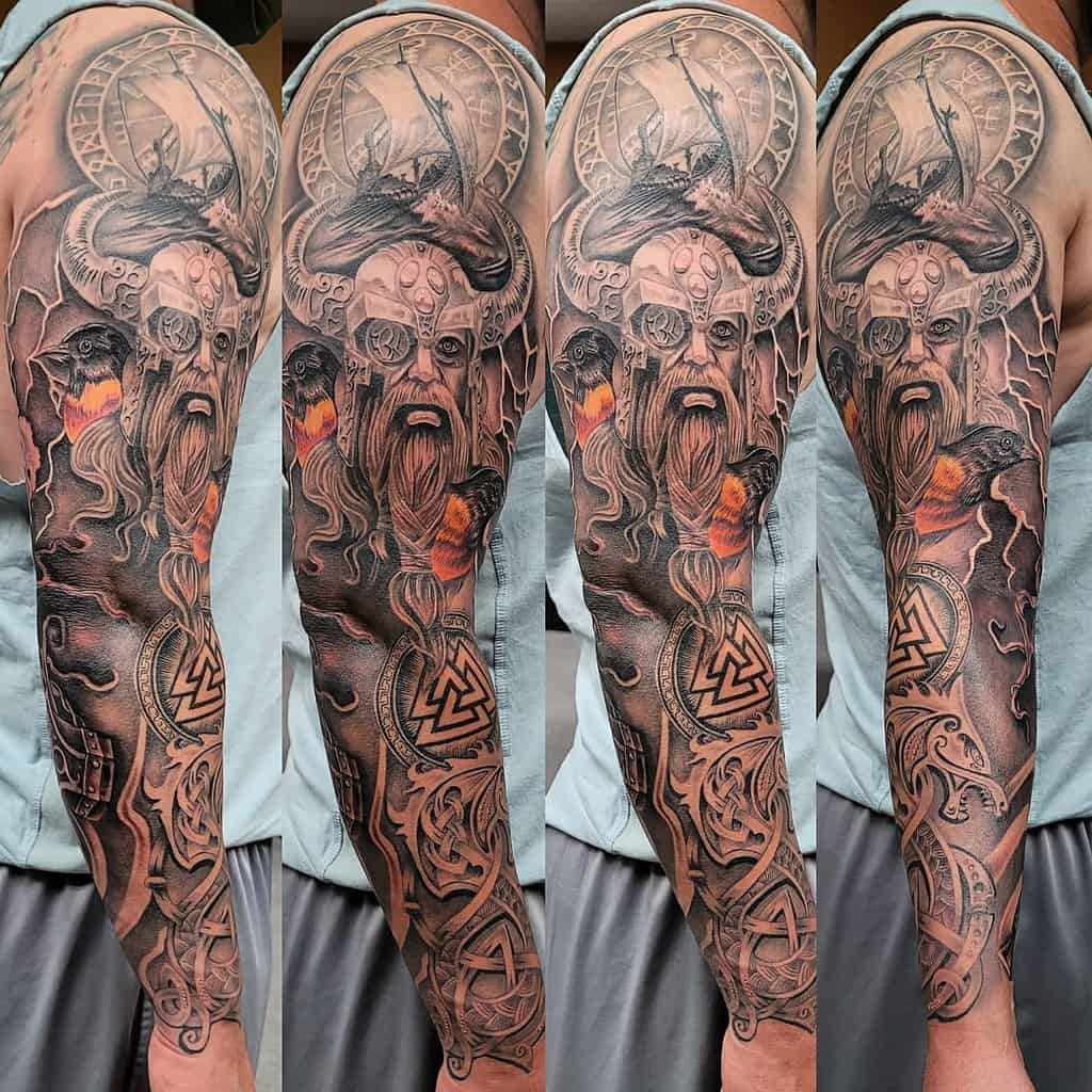 A detailed full-sleeve tattoo featuring a Viking warrior with a horned helmet, ravens, lightning, the Valknut symbol, and intricate knotwork, with accents of orange