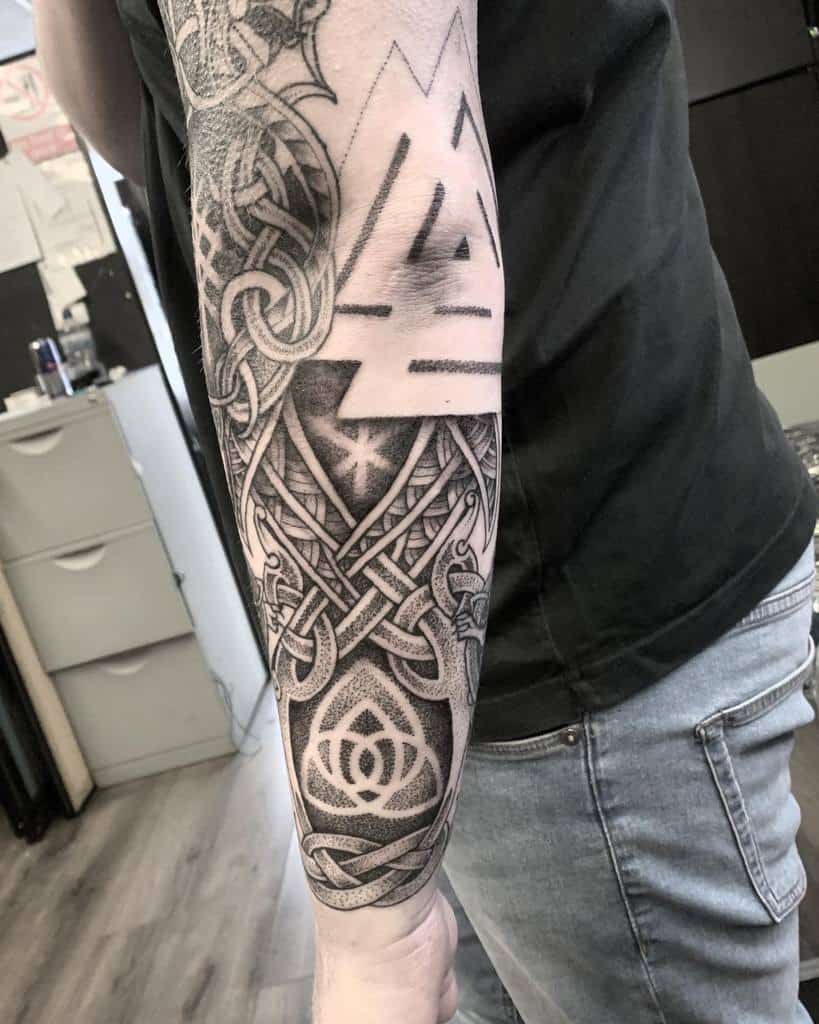 A forearm tattoo featuring the Valknut symbol, intricate knotwork, and geometric patterns in a detailed dotwork style