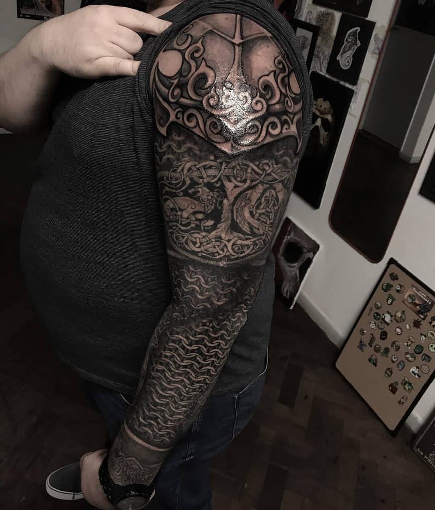 A full-sleeve tattoo featuring bold Nordic designs with intricate knotwork, mythical creatures, and layered wave patterns, extending from shoulder to wrist