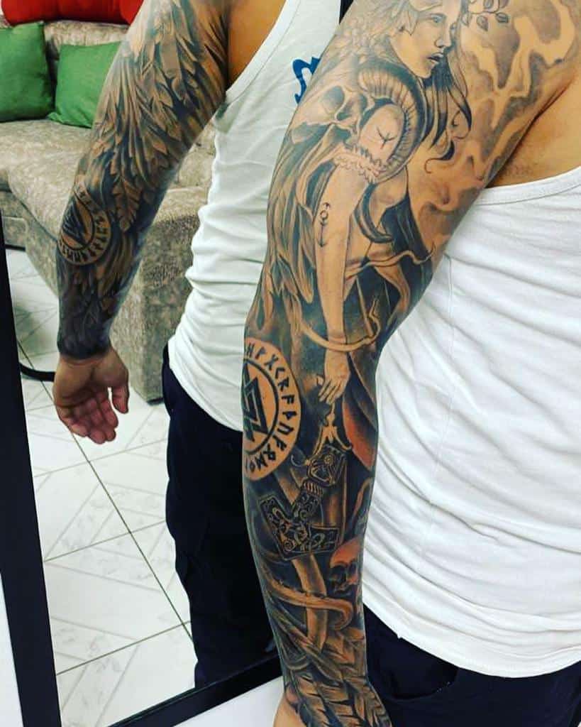 A full-sleeve tattoo featuring a Valkyrie, Norse runes, wings, and detailed Viking symbolism, with elements of fire and smoke throughout