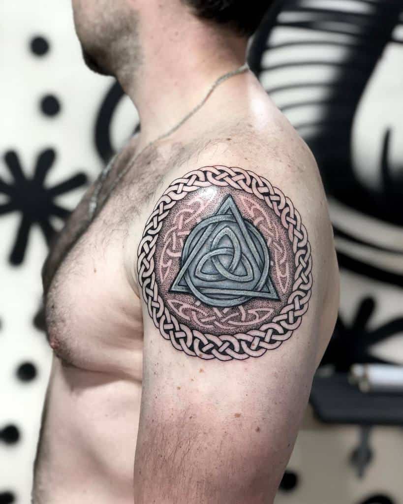 Man with a Celtic knot tattoo on his upper arm, featuring a triangular design surrounded by braided patterns