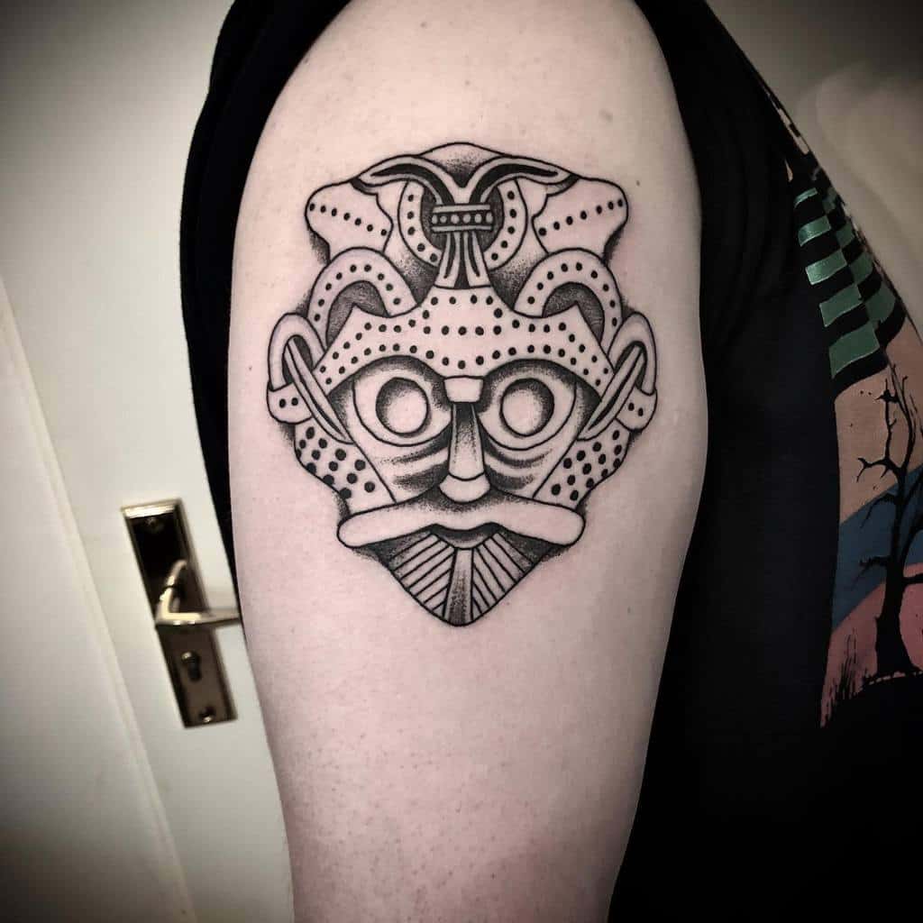 Nordic-inspired upper arm tattoo of a stylized Viking mask with geometric details and dotwork shading