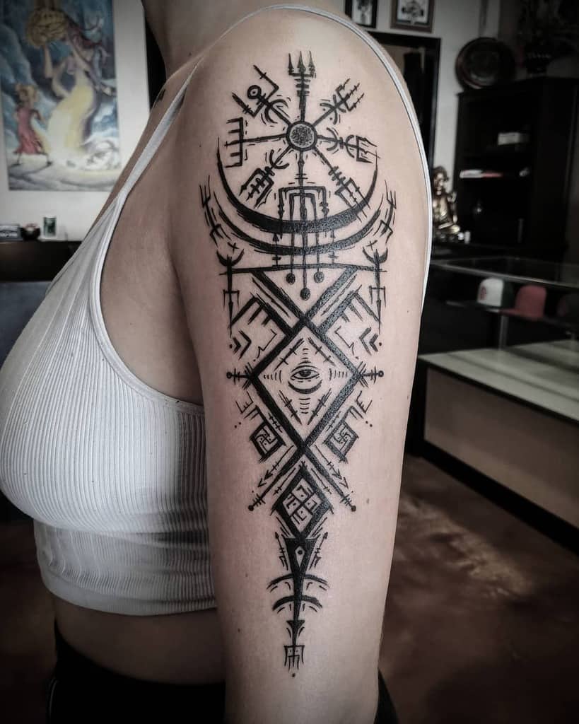 Nordic-inspired upper arm tattoo featuring symbolic patterns, geometric shapes, and a crescent moon with a central eye