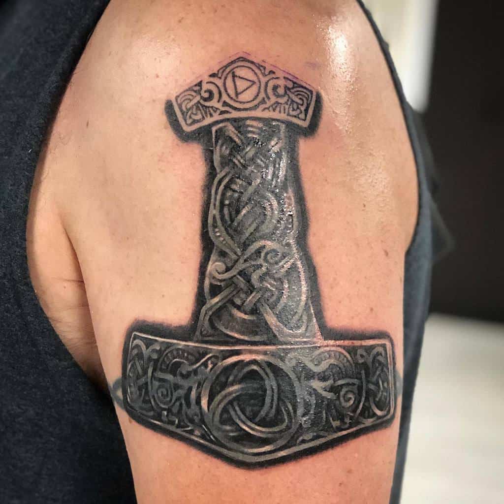 Upper arm tattoo of a Mjolnir hammer with intricate Celtic knot designs and Norse symbols