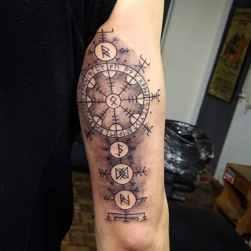 Tattoo of a Norse runic compass with runes below on an upper arm, detailed in black ink