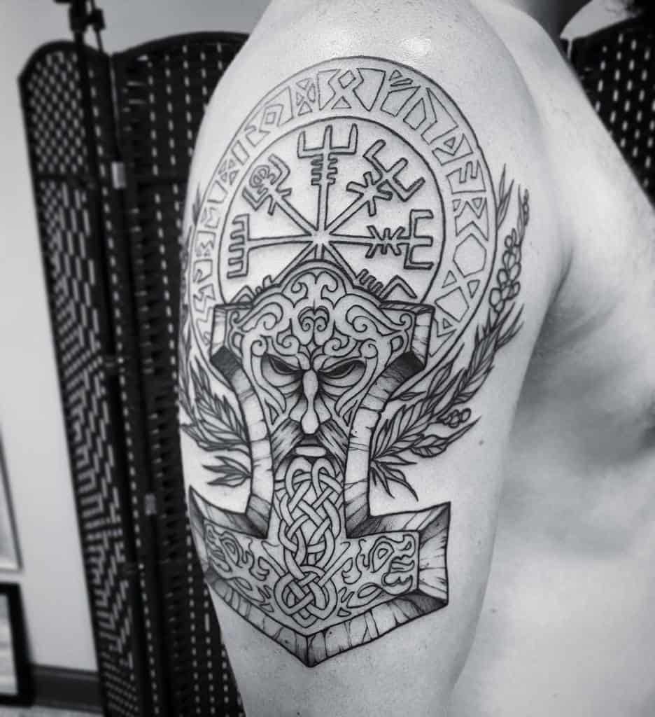 Detailed Norse mythology-themed tattoo on upper arm featuring runes, a helmeted face, and intricate knotwork designs