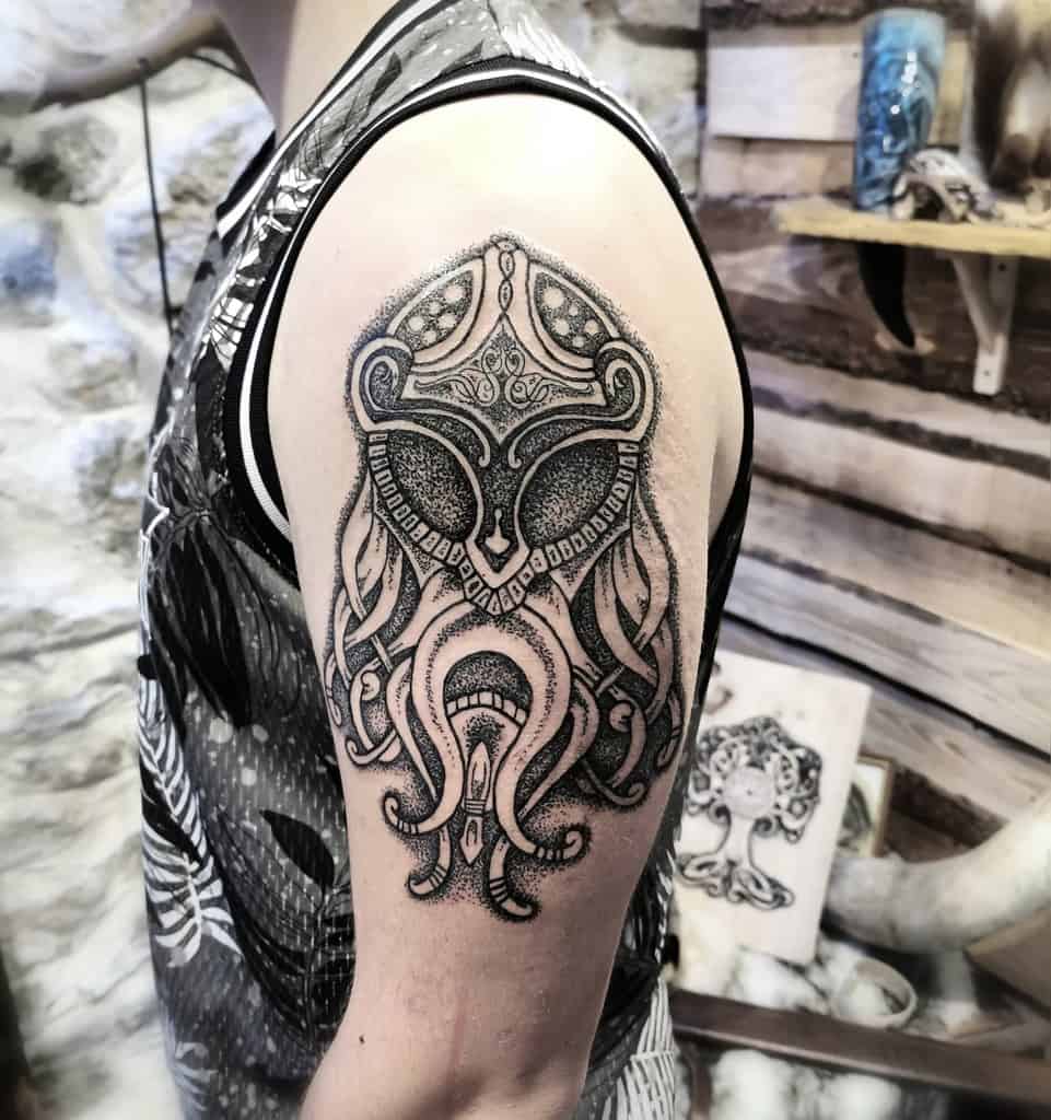 Upper arm tattoo of a detailed Norse helmet and intricate knotwork, in black and gray ink