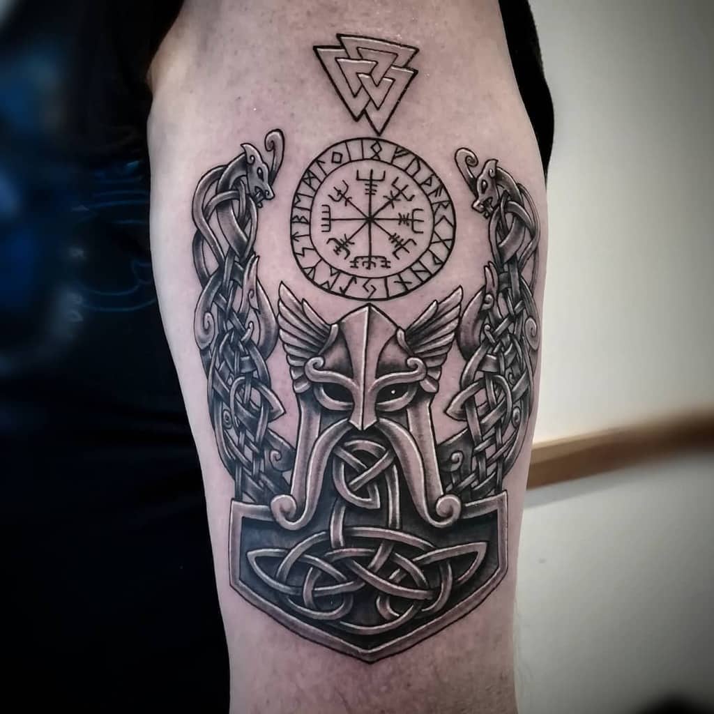Nordic upper arm tattoo featuring a Viking helmet with intricate knotwork designs, runes, and a Vegvisir compass symbol above