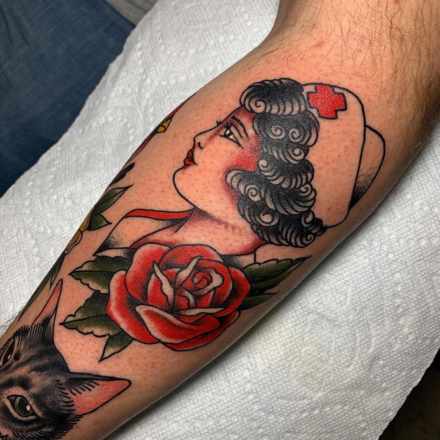 Tattoo of a nurse with a red cross and roses on a calf