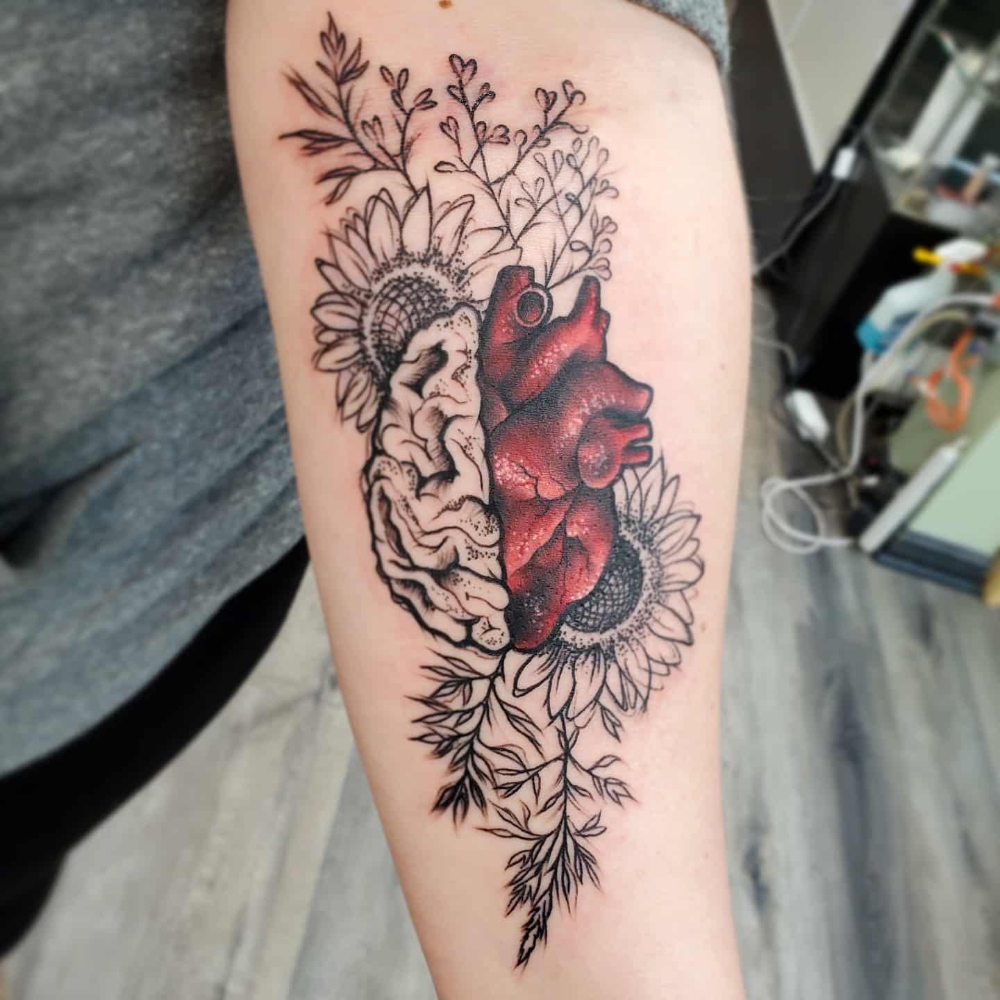 Tattoo of a heart and brain with sunflowers and foliage on a forearm