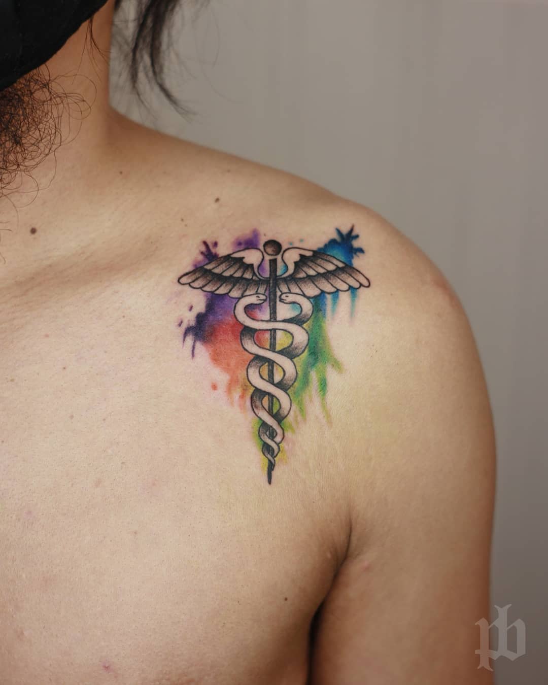 Caduceus tattoo with colorful background on upper chest near shoulder