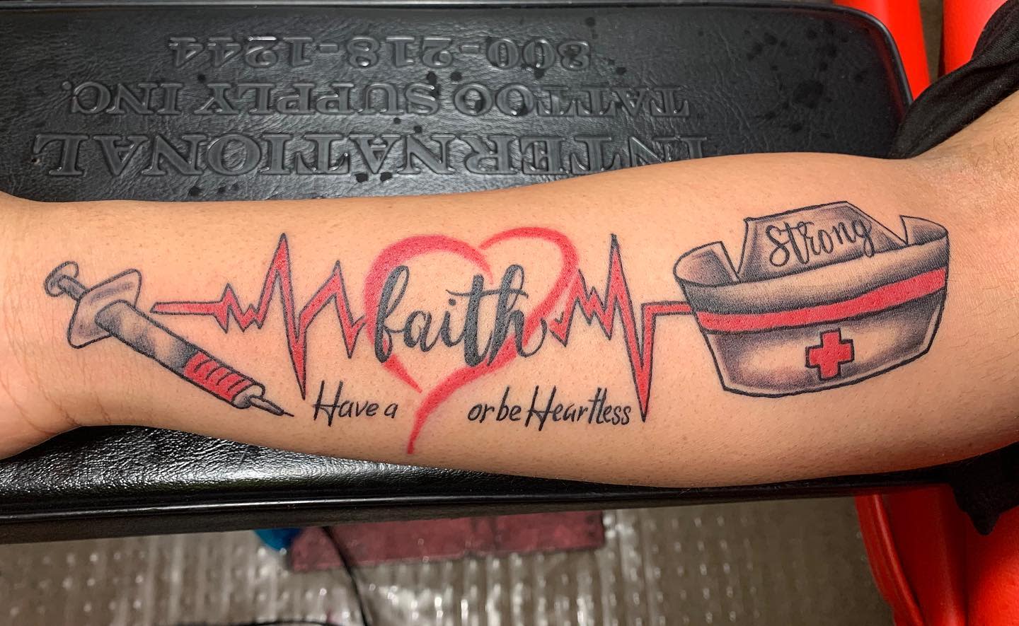 Forearm tattoo with medical symbols, heart, EKG line, and text "faith" and "strong"