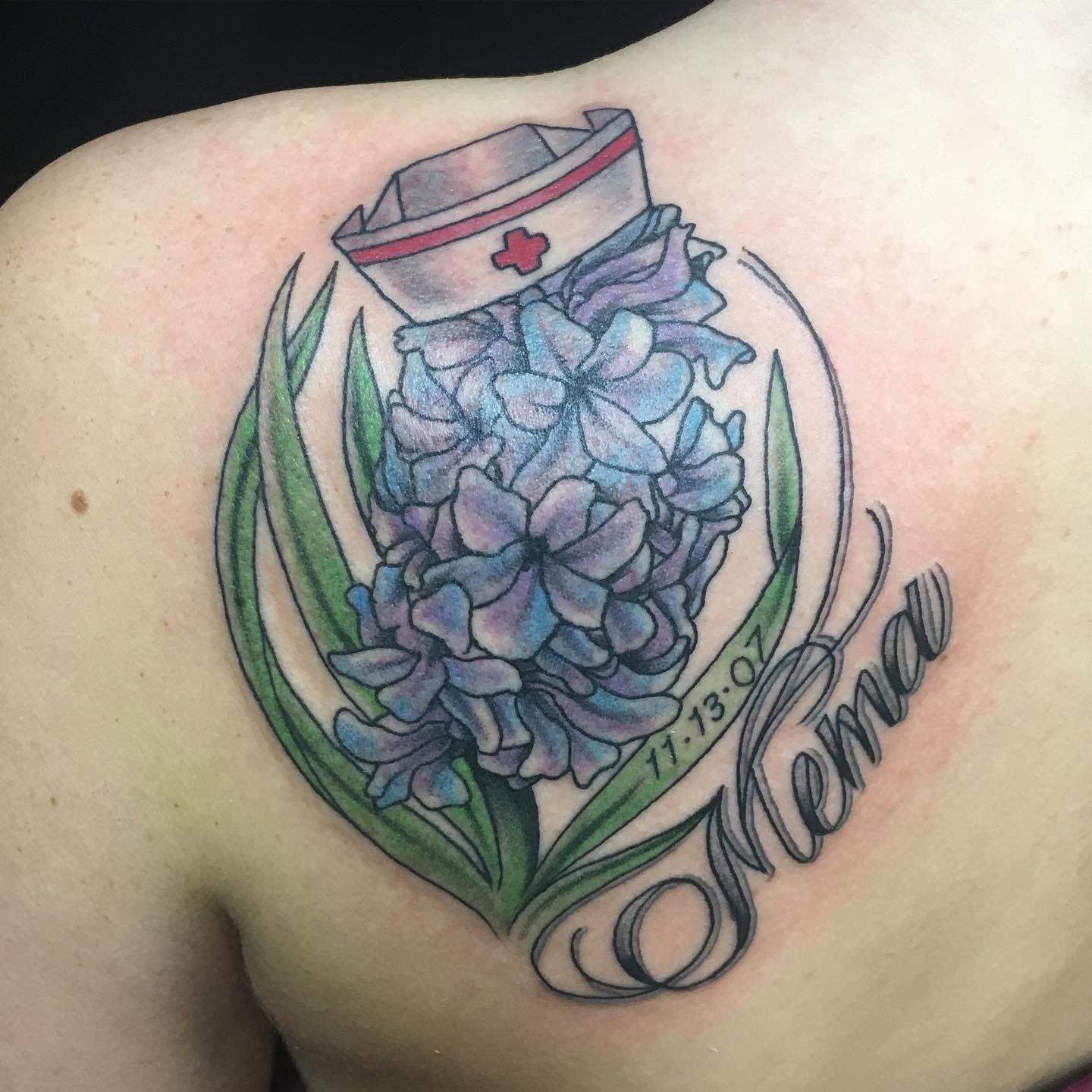 Tattoo of a purple flower, nurse cap, and "Mema" with a date on a shoulder