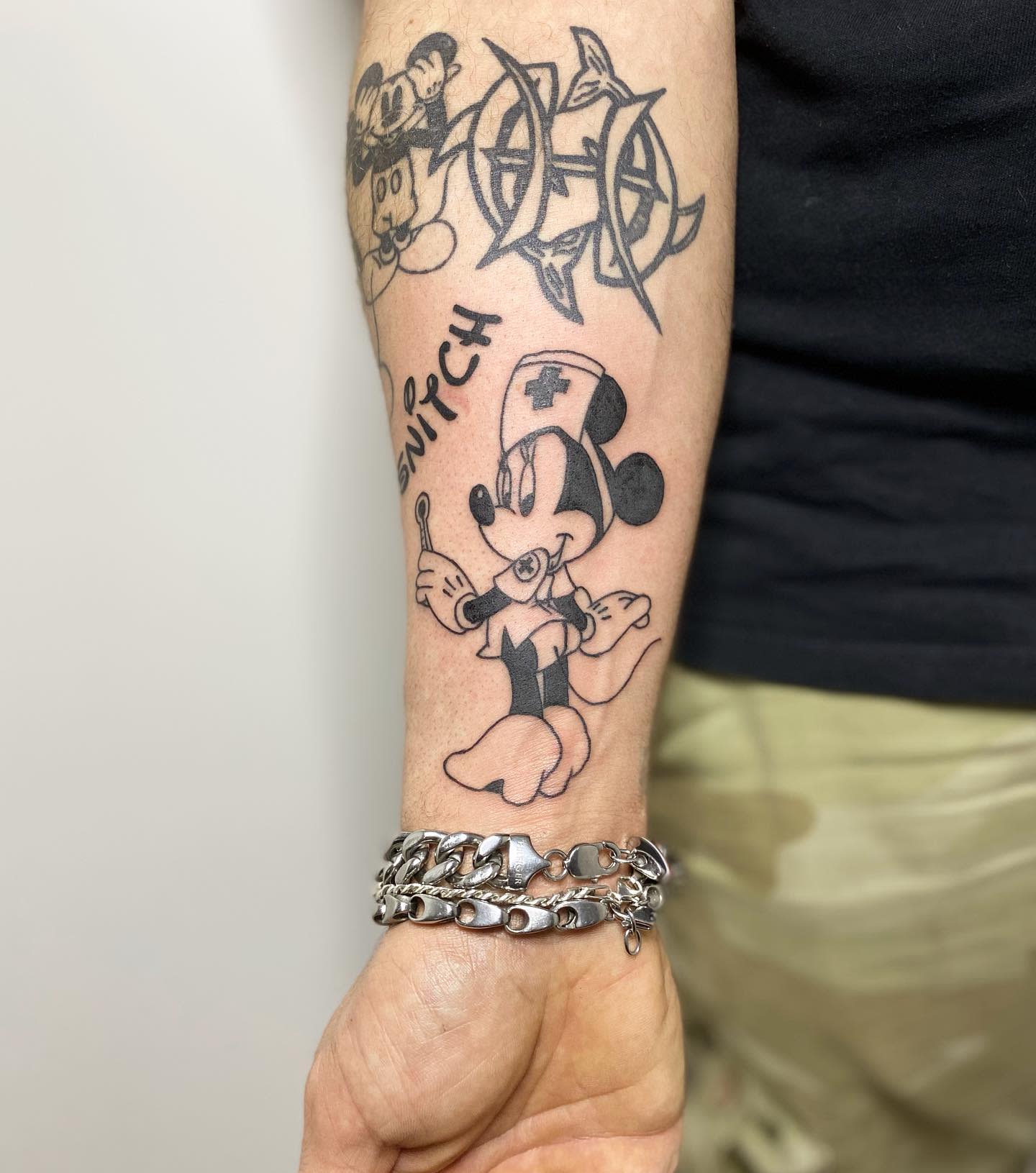 Forearm tattoos: a nurse's mouse, tribal design, and cartoon mouse face with a chain bracelet