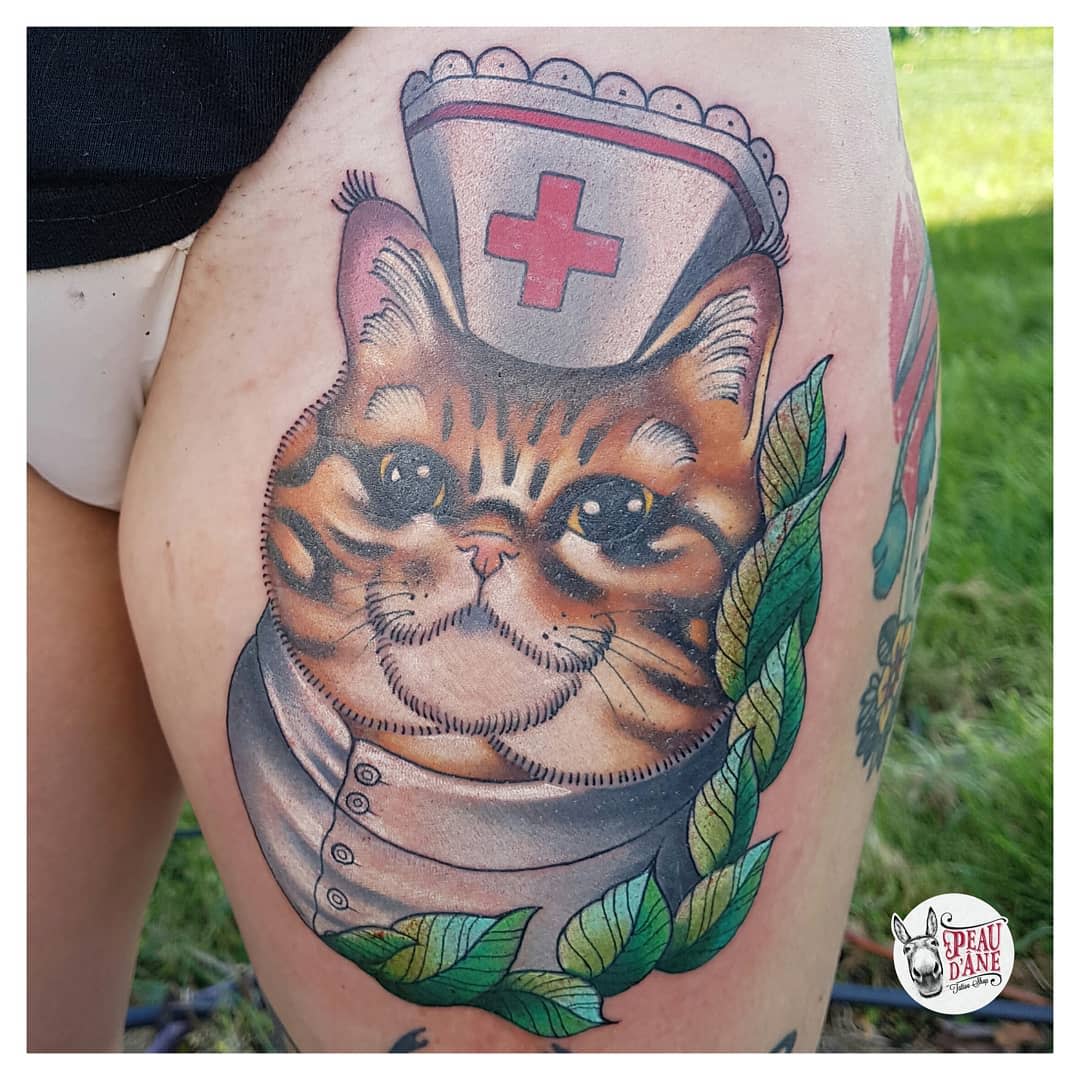 Tattoo of a nurse cat with a red cross hat, on an upper thigh