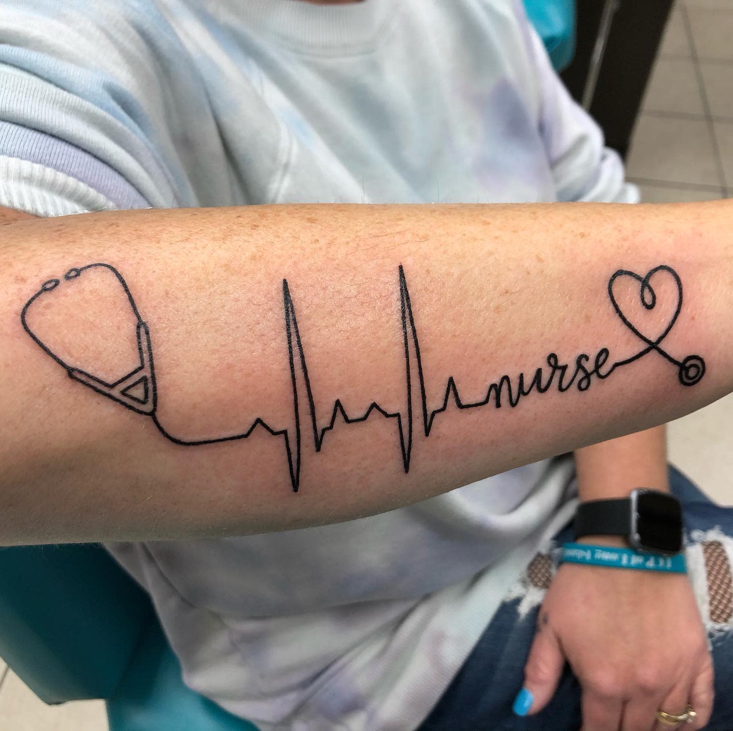 Tattoo of a stethoscope, heartbeat line, and the word "nurse" with a heart on an arm