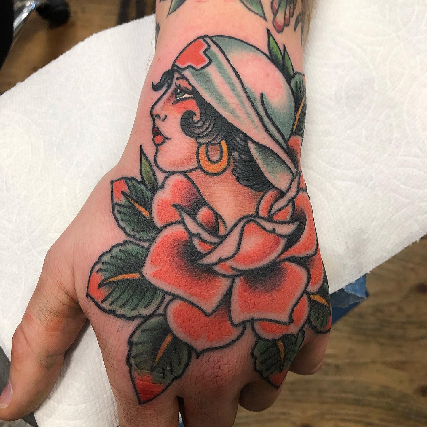 Hand tattoo featuring a woman with a headscarf surrounded by a large rose and leaves