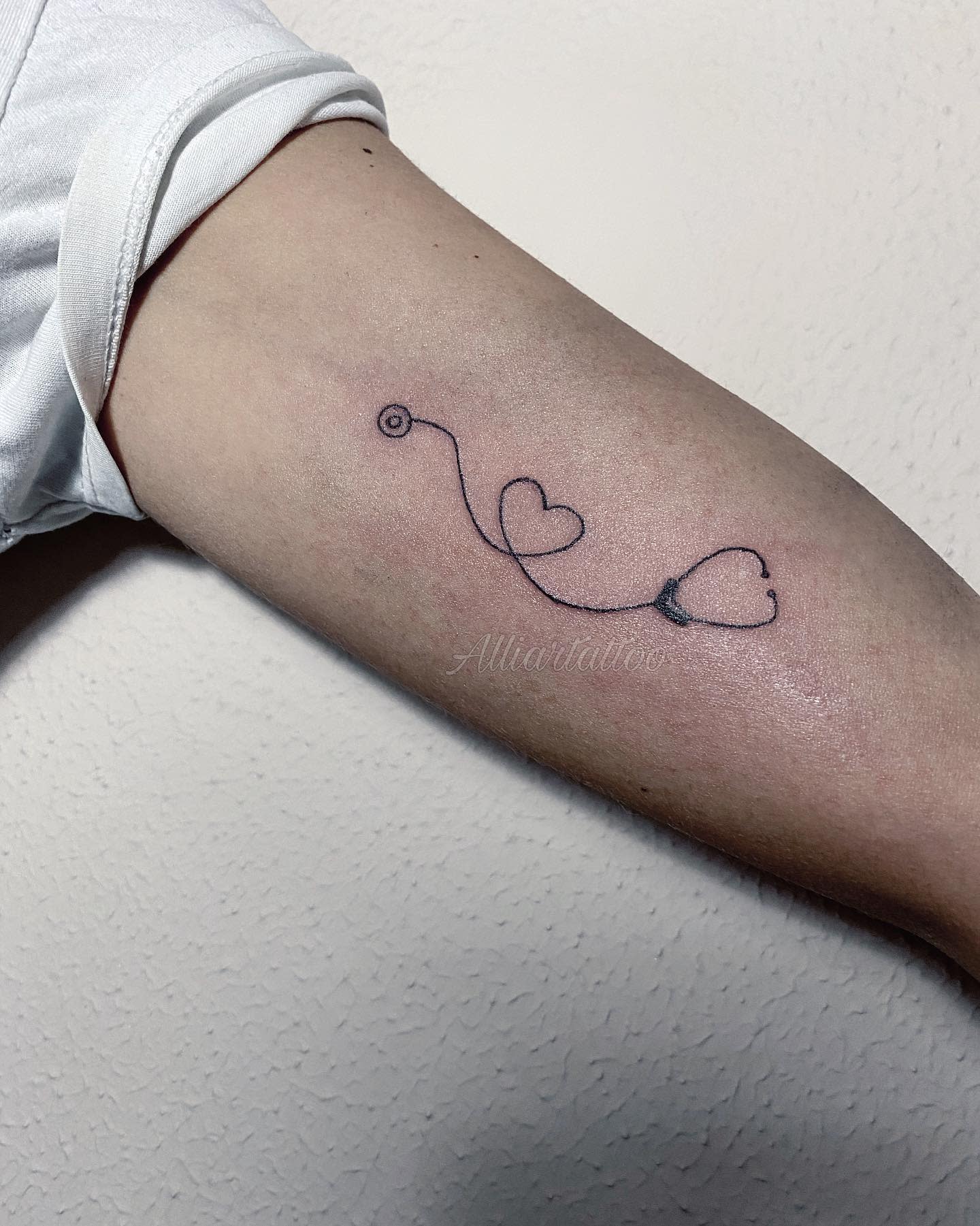 Simple line tattoo of hearts connected by a stethoscope on an inner forearm