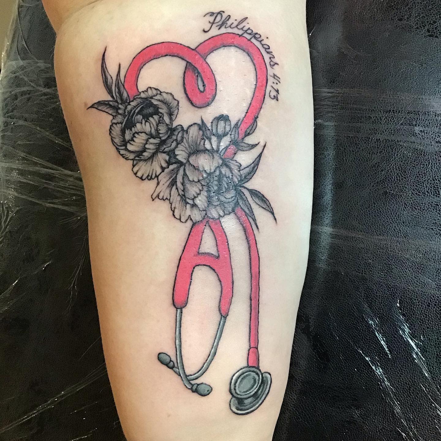 Tattoo of a stethoscope forming a heart with flowers and "Philippians 4:13" text