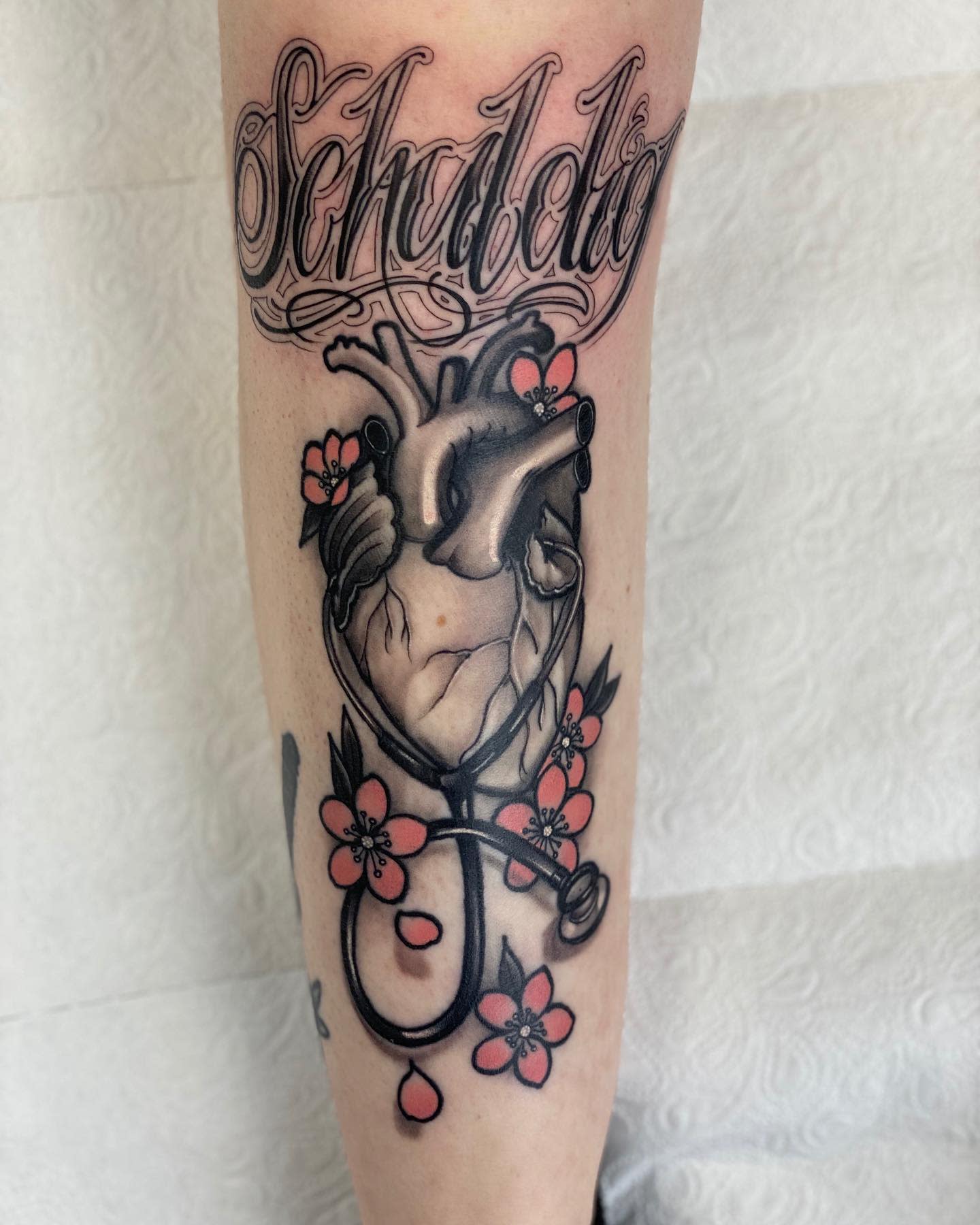 Tattoo of a heart with flowers, a stethoscope, and "Schroda" written above it