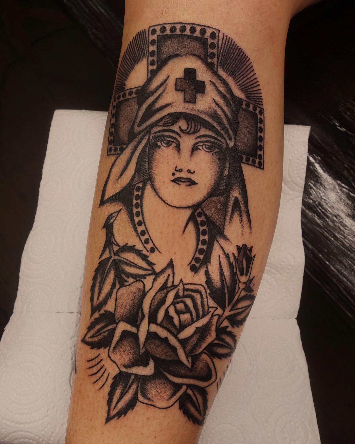 Black and grey tattoo featuring a nurse and a rose below