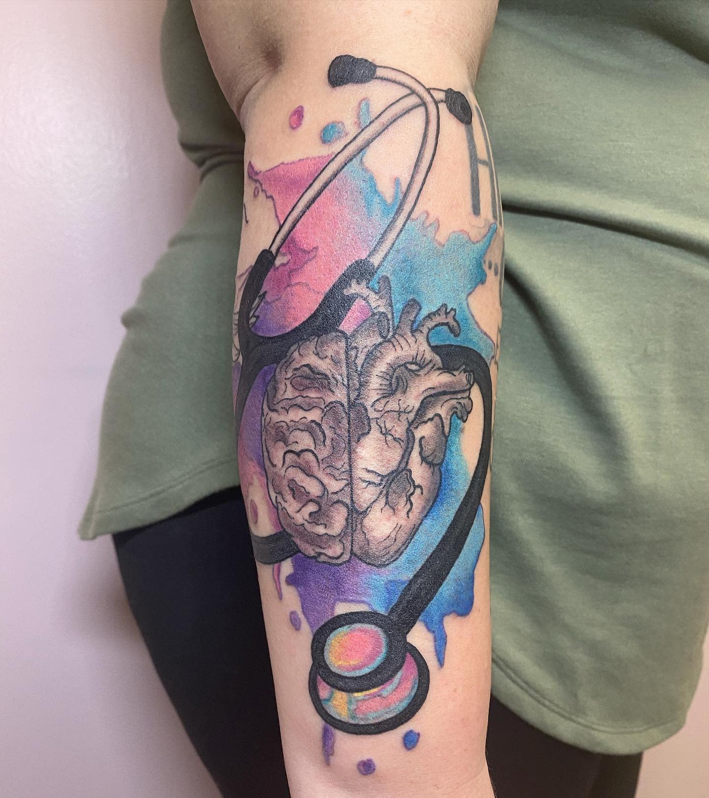 Tattoo of a heart and stethoscope with colorful splashes on the forearm
