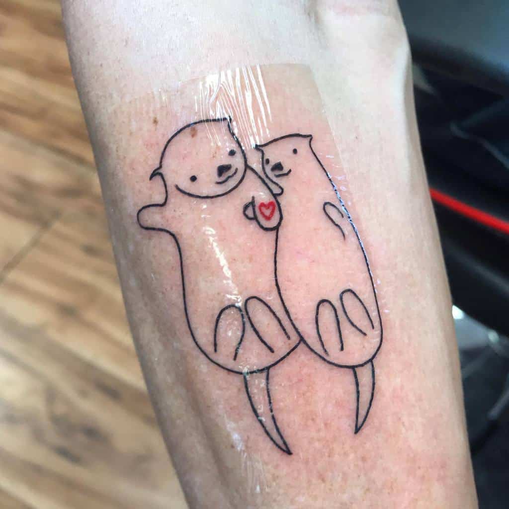 Tattoo of two adorable otters holding hands with a heart between them
