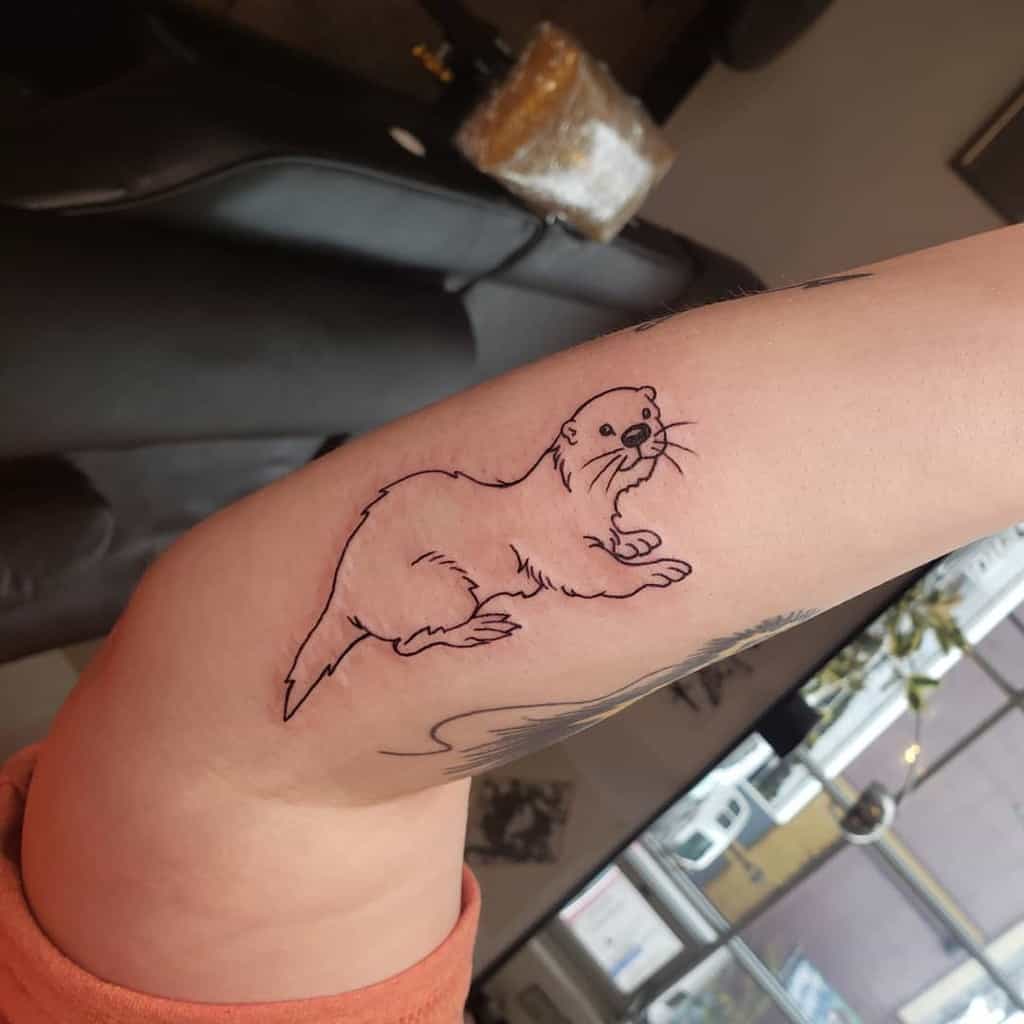 Otter tattoo graces an arm, featuring a sleek outlined design with minimal shading
