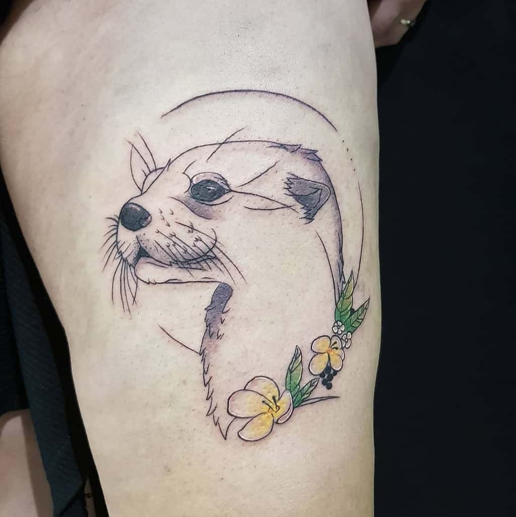 Tattoo of a playful otter outlined in a circle, adorned with vibrant yellow flowers and lush green leaves