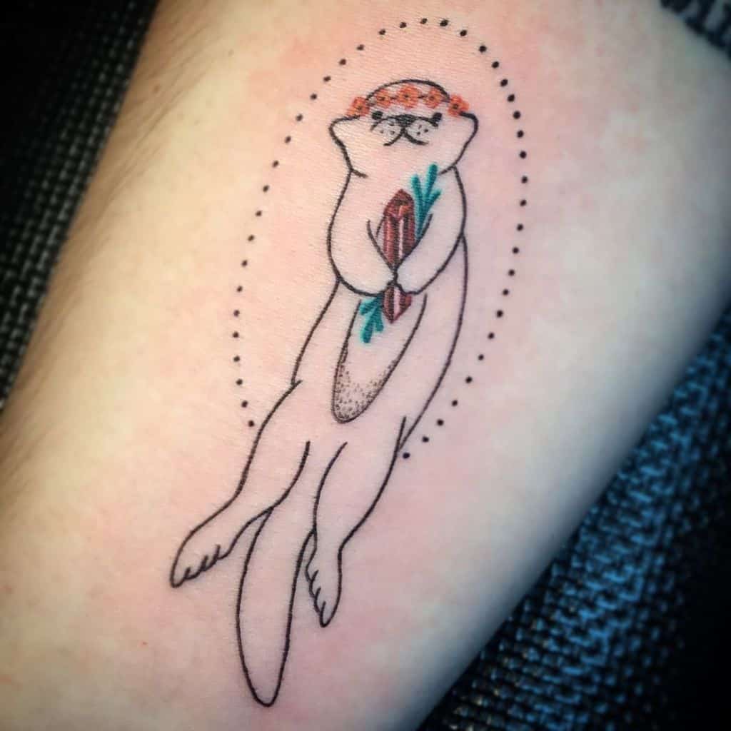 Tattoo of an adorable otter clutching a surfboard, surrounded by artistic dotted lines on skin