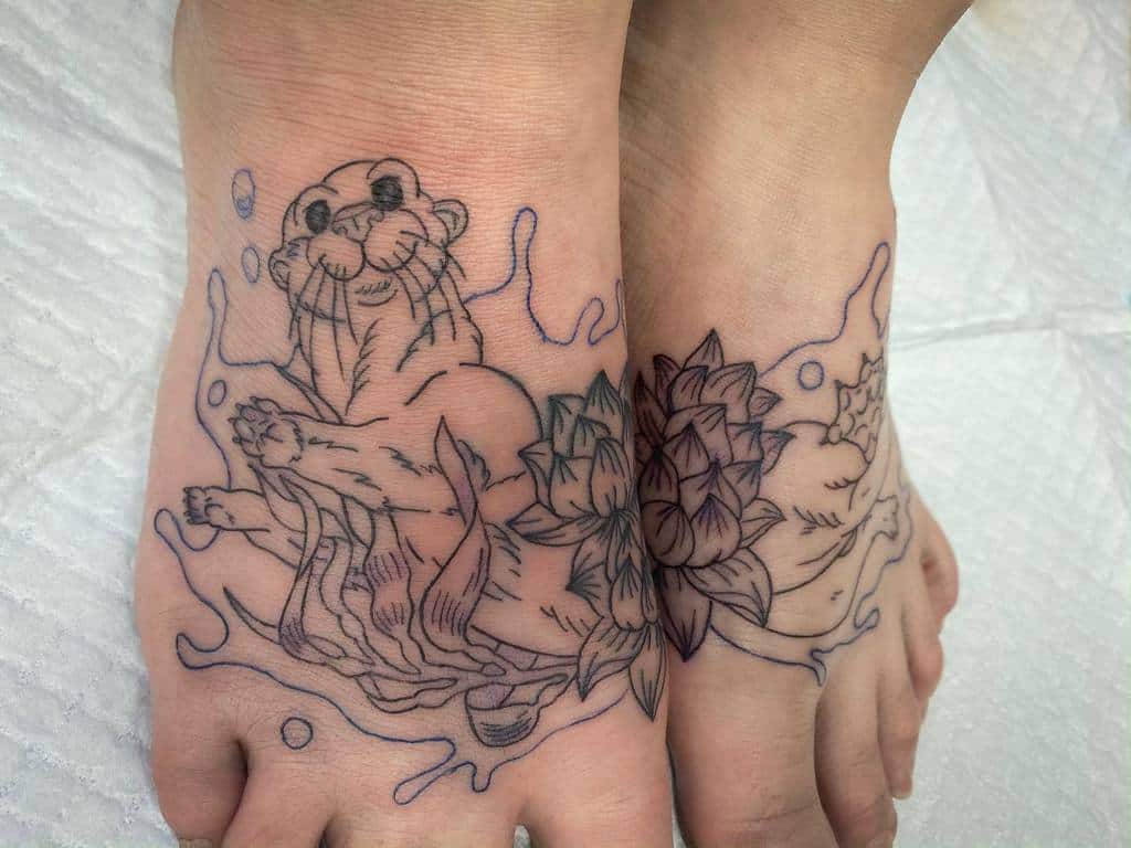 Whimsical foot tattoo with playful otters, lotus flowers, and water splashes; detailed lines bring the scene to life