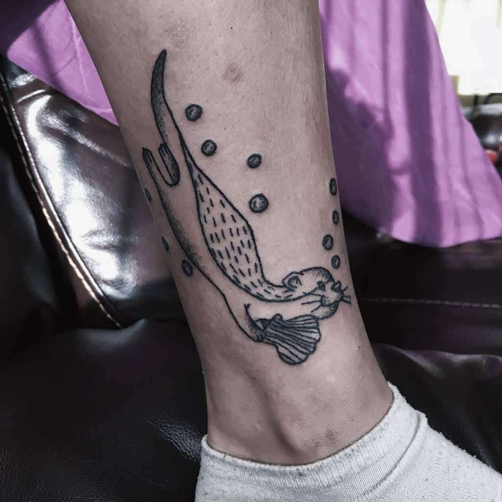 Tattoo of a playful otter, clutching a shell amidst bubbles