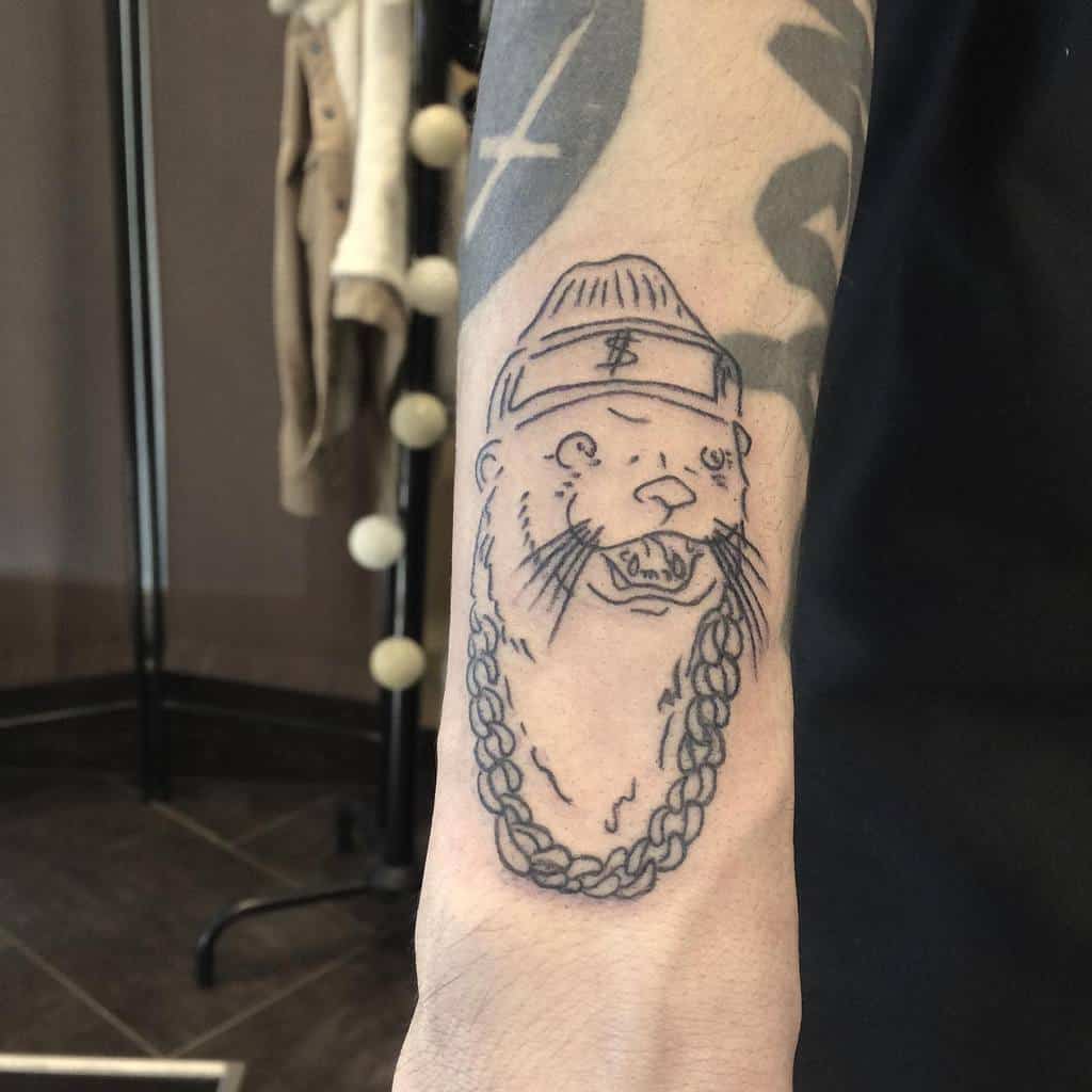 Otter tattoo with a beanie, dollar sign, and chunky chain adorns the forearm