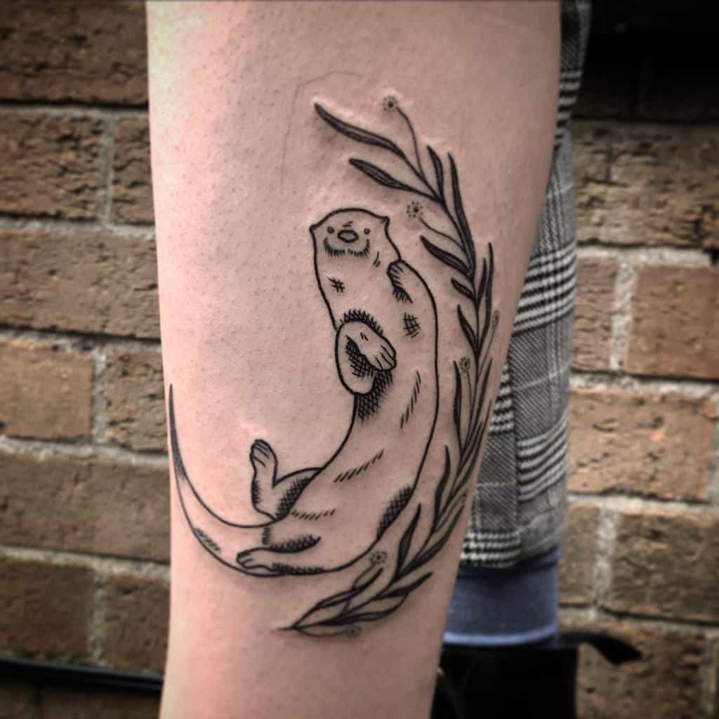 Playful otter tattoo clutching a leafy branch on a forearm
