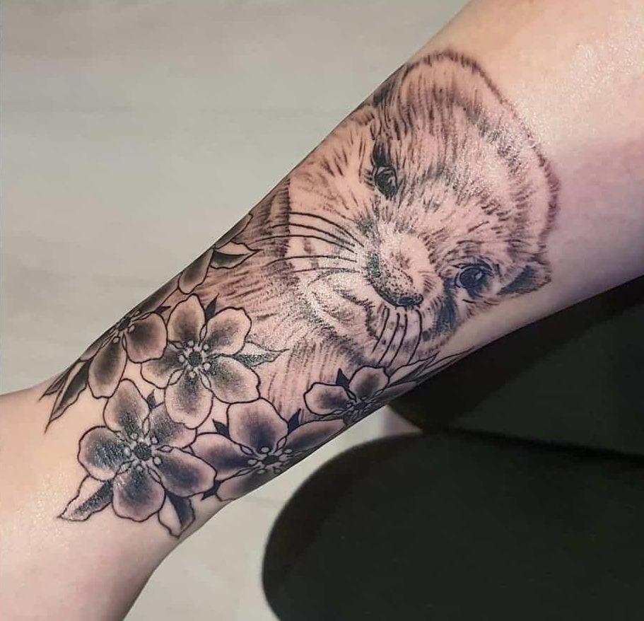 Tattoo of an otter's face and cherry blossoms on a forearm