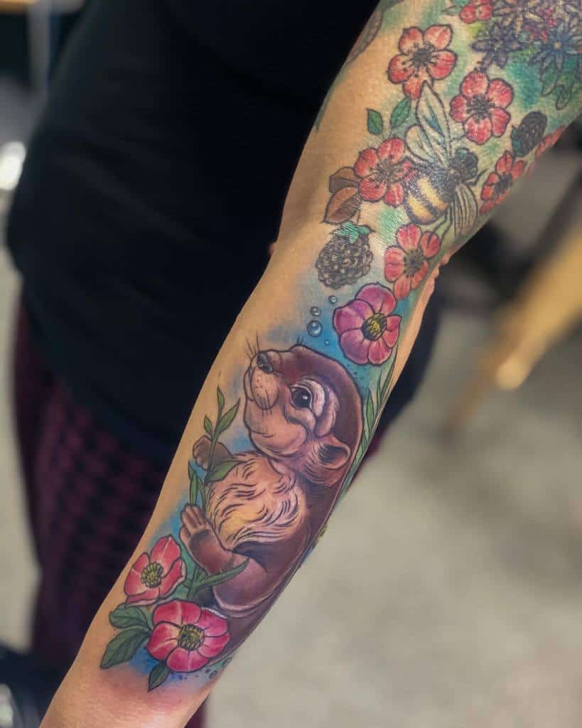 Forearm tattoo of an otter surrounded by colorful flowers and leaves, with bubbles above its head