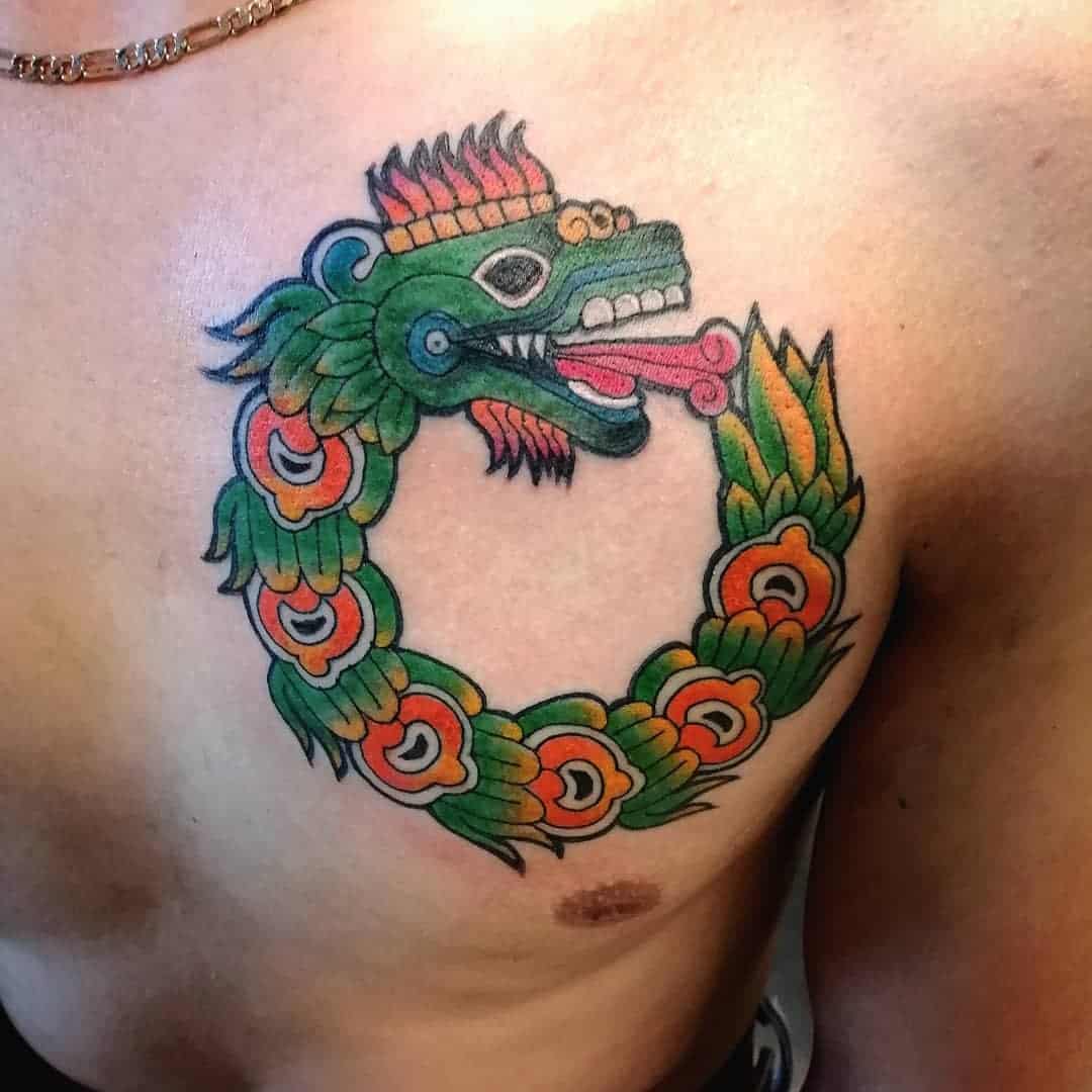 A vibrant Ouroboros-style Quetzalcoatl tattoo on the chest, featuring a colorful, feathered serpent biting its tail, symbolizing eternity and the cyclic nature of life
