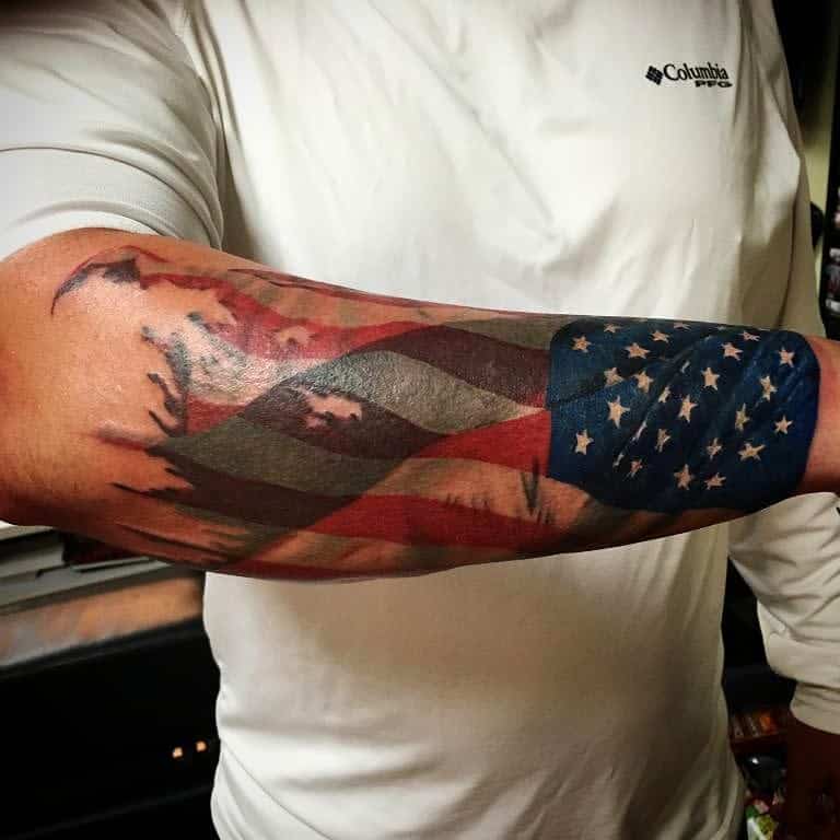 Tattoo of a tattered American flag on the outer forearm of a man