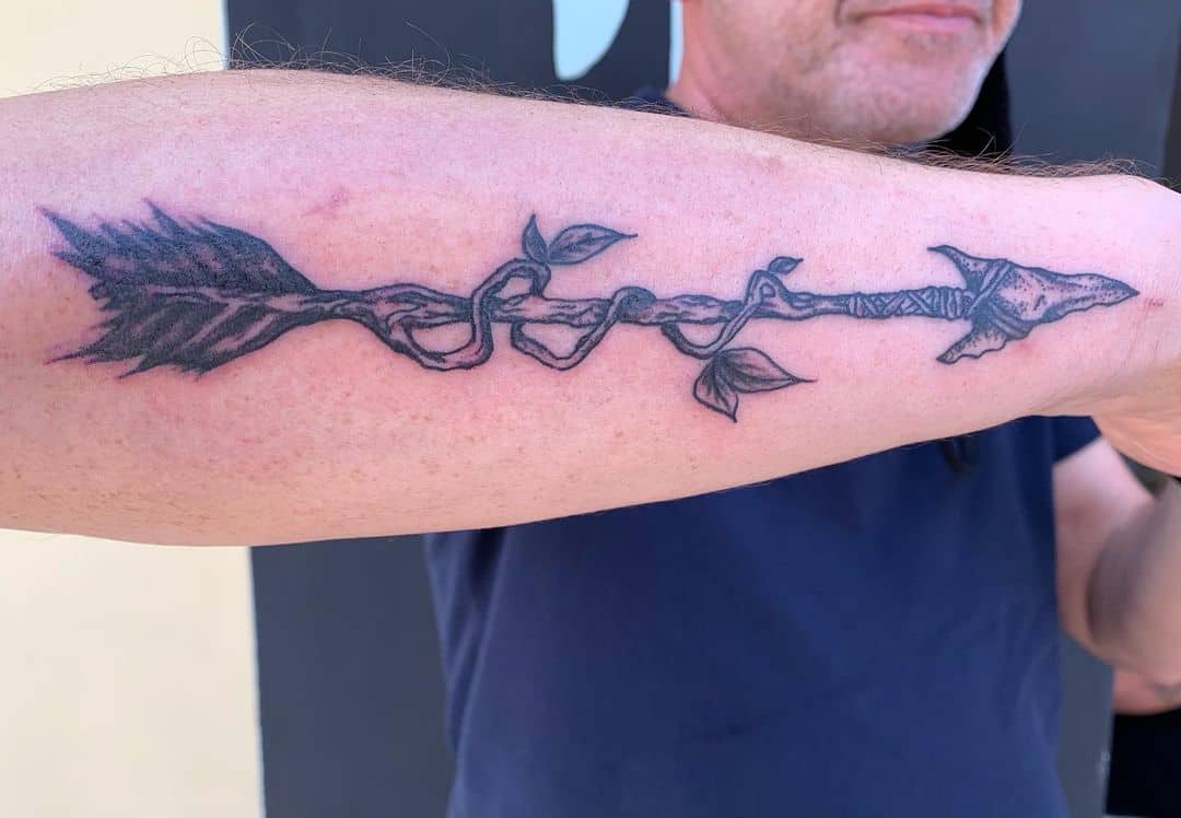 Outer forearm tattoo of an arrow entwined with twisting vines and leaves