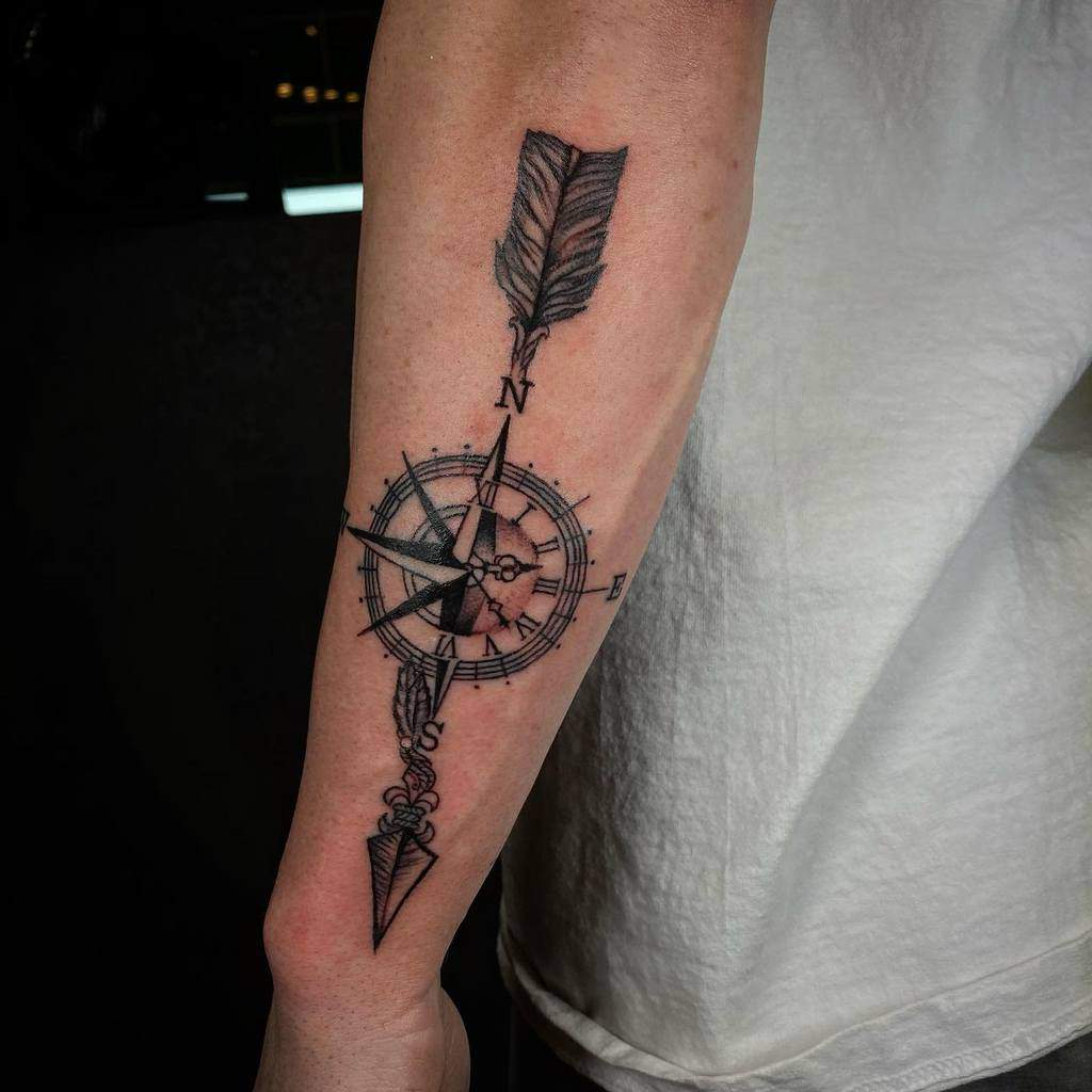 Outer forearm tattoo featuring a detailed compass with an arrow pointing north, symbolizing direction, guidance, and adventure
