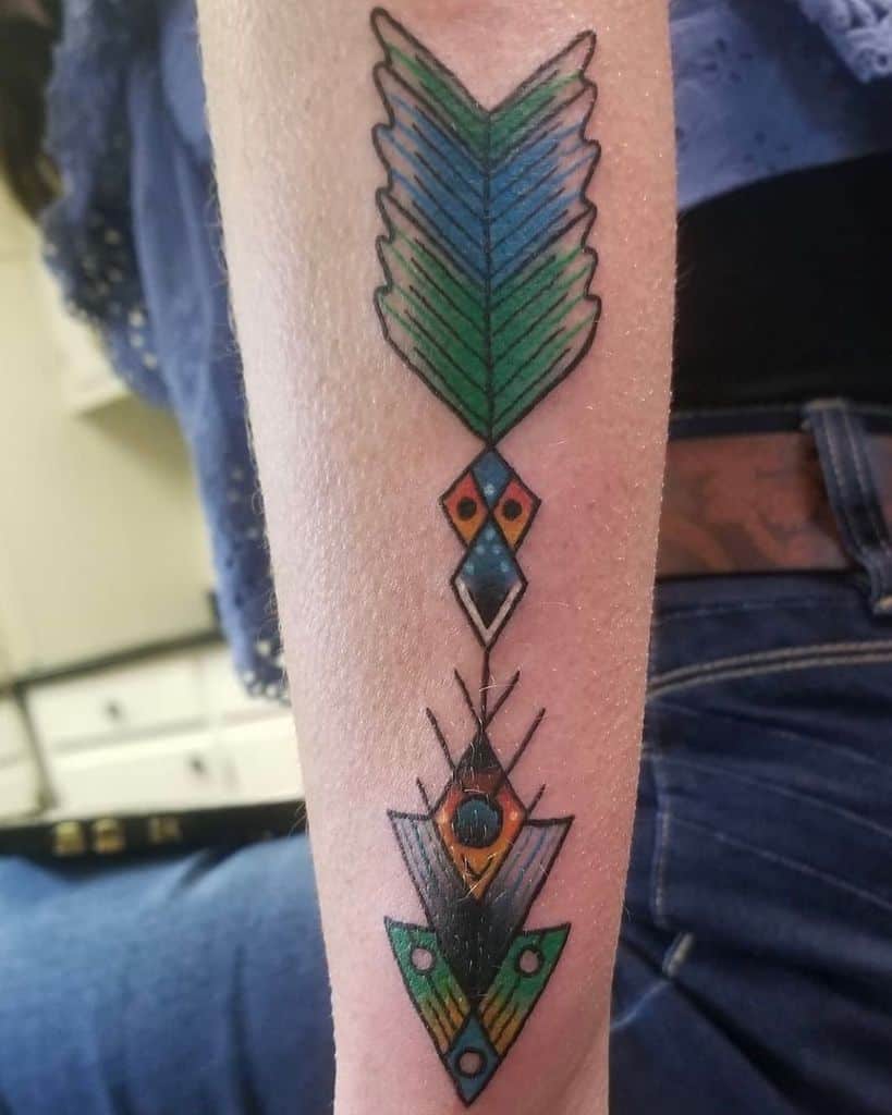 A colorful geometric tattoo graces the outer forearm, showcasing arrow-like shapes and vivid patterns