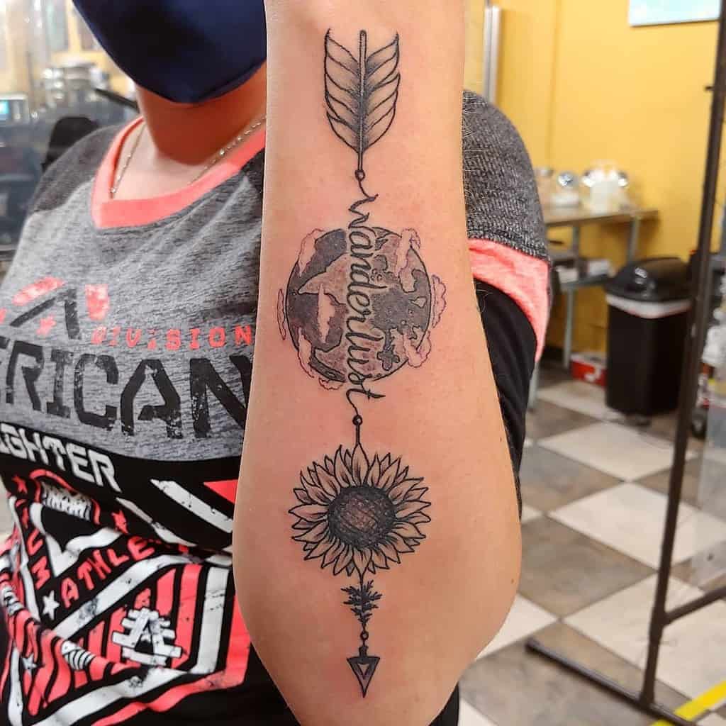Outer forearm tattoo featuring an arrow, a sunflower, and a globe with the word 'wanderlust,' symbolizing a love for travel and nature