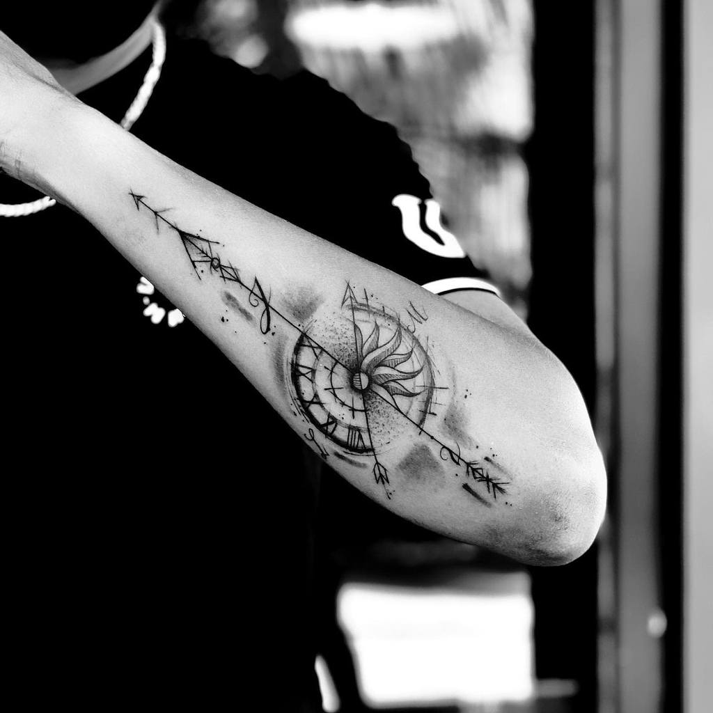 A black and white tattoo of a clock and abstract design elegantly graces the outer forearm