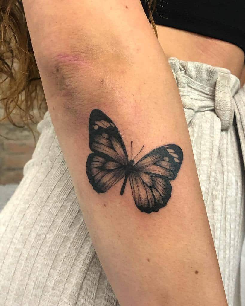 A realistic butterfly tattoo graces the outer forearm, resting elegantly near the elbow